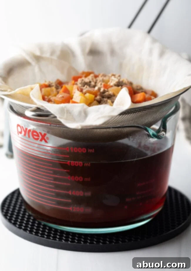 A strainer holding the consomme raft over a liquid measuring cup.