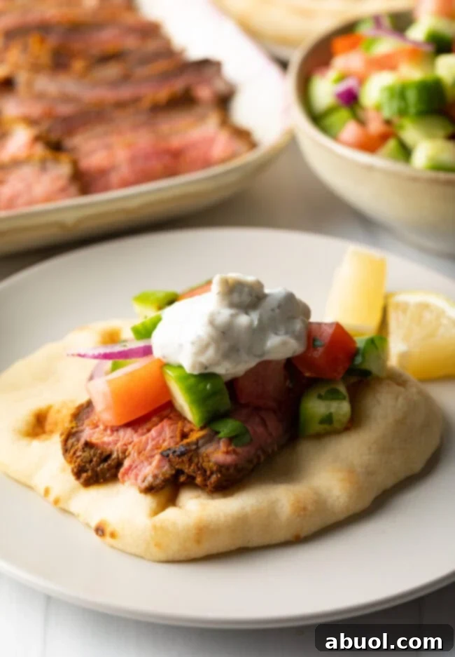Savory Spiced Beef Shawarma 2 Close view flatbread naan beef shawarma wrap topped with chopped cucumbers, tomatoes, red onion and tzatziki sauce.