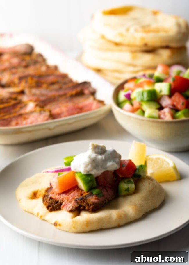 Savory Spiced Beef Shawarma 13 Close view flatbread naan beef shawarma wrap topped with chopped cucumbers, tomatoes, red onion and tzatziki sauce.