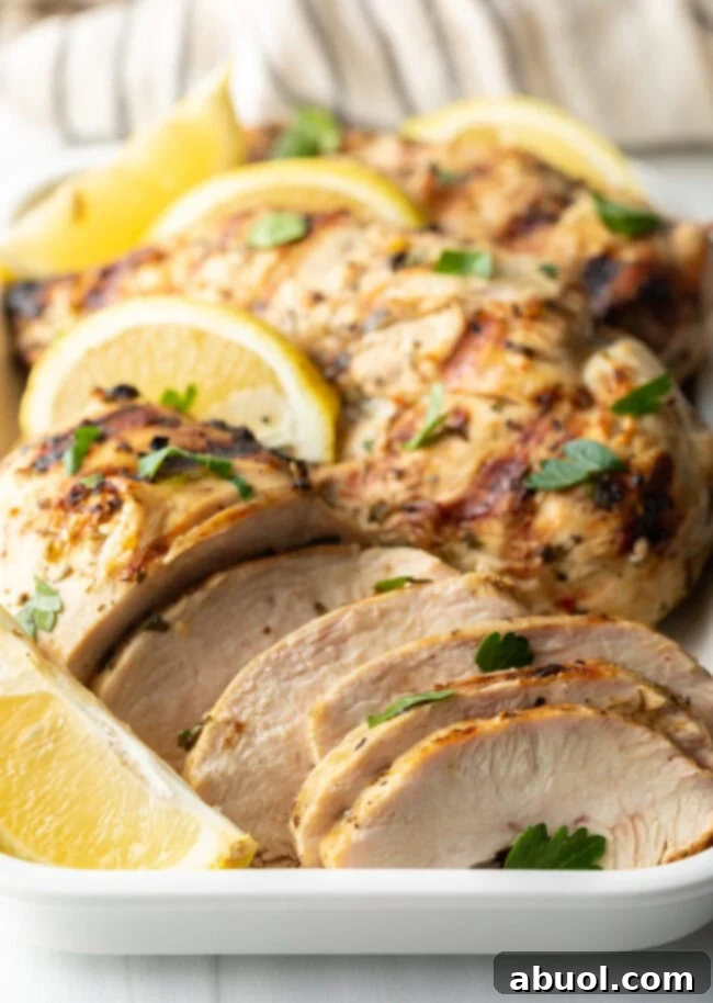 Close-up view of succulent, marinated grilled chicken pieces garnished with fresh lemon wedges on a pristine white serving platter.