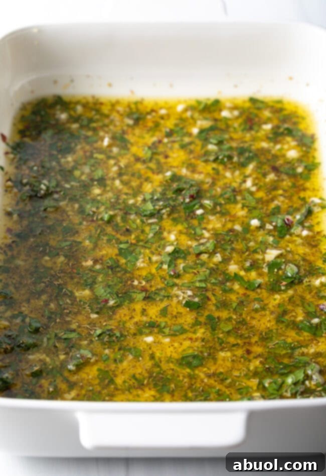 The fully mixed Greek marinade, a vibrant and aromatic blend, resting in a white baking dish.