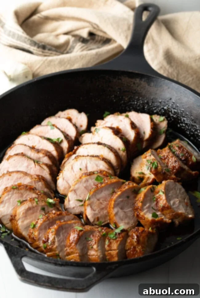 Slices of perfectly roasted honey garlic pork tenderloin, glistening with glaze, arranged in a rustic black cast iron pan, ready to be served.