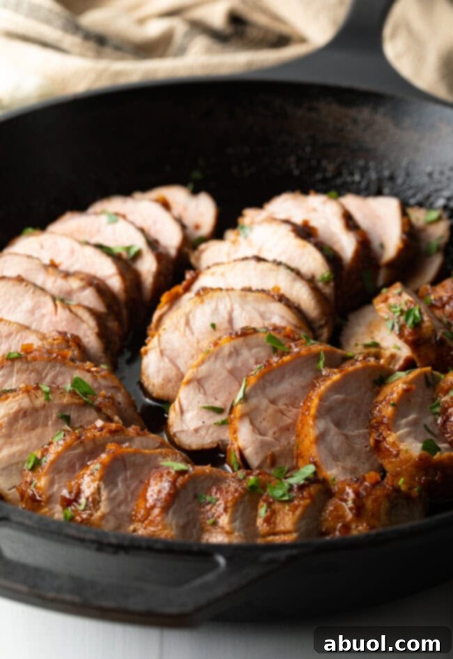 Slices of succulent slow cooker honey garlic pork tenderloin, glistening with its rich sauce, served elegantly in a black cast iron pan.