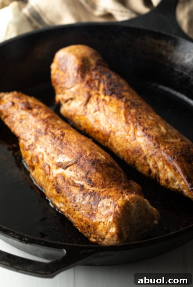 Two perfectly seared pork tenderloins, golden brown, resting in a black cast iron skillet before glazing.