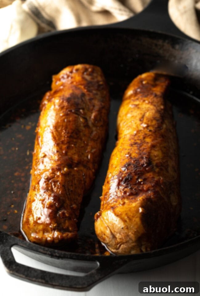 Two seared pork tenderloins simmering in the rich honey garlic glaze within a cast iron skillet, ready for the oven.
