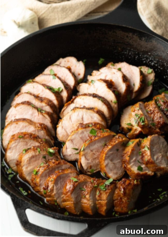 Tender slices of slow cooker honey garlic pork tenderloin, glistening with sauce, artfully arranged in a black cast iron pan.