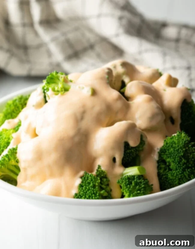 Generous bowl of vibrant steamed broccoli florets completely covered in homemade cheddar cheese sauce.