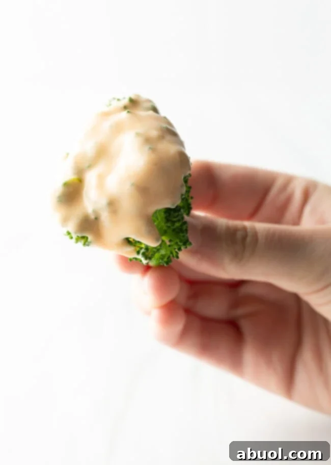Hand holding a fresh broccoli floret generously coated with homemade cheese sauce.