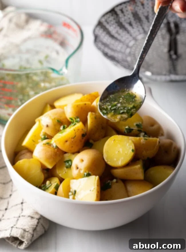 Metal spoon with garlic herb butter, drizzling over steamed potatoes in a white bowl.