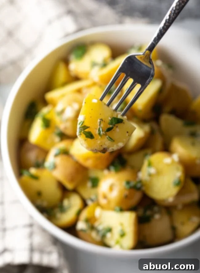 Fork with halved baby potato coated in garlic herb butter, shown to camera.