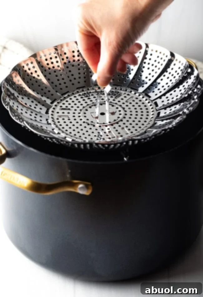 Hand adding metal steaming basket to a large black stock pot.