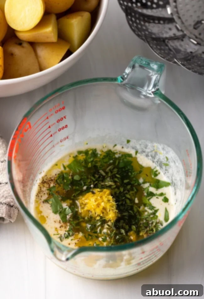 Glass measuring pitcher with melted butter, fresh chopped herbs, spices, and lemon zest.