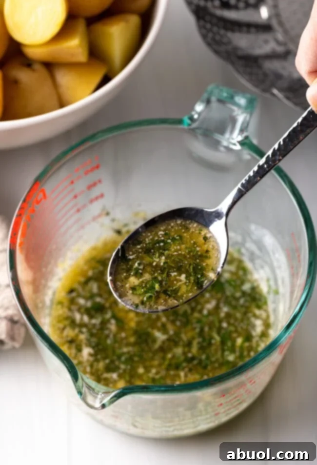 Spoon with garlic herb butter shown to camera, above the glass measuring pitcher.