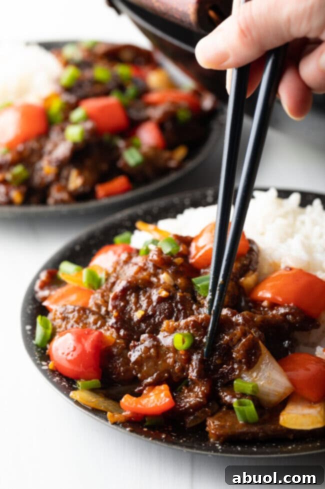Sweet and Crispy Panda Express Beijing Beef 13 A hand holding black chopsticks picks up a piece of crispy Beijing Beef from a bowl filled with stir-fry and rice.