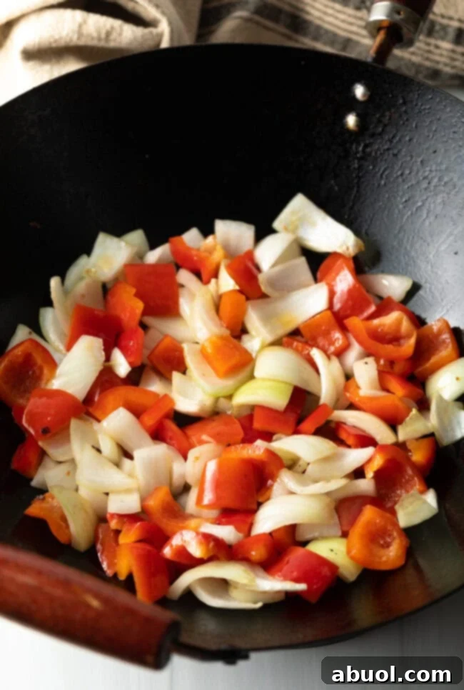 Sweet and Crispy Panda Express Beijing Beef 9 Raw, chopped bell peppers and onions sizzling in a hot skillet during the stir-frying process.
