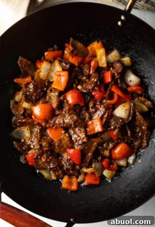 Sweet and Crispy Panda Express Beijing Beef 10 A top-down view of stir-fried beef and colorful vegetables coated in sauce within a wok.