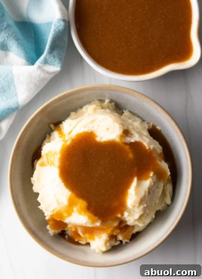 Delicious Homemade Beef Gravy 3 Top down bowl of mashed potatoes covered with beef gravy, with white pitcher of more gravy in the background.