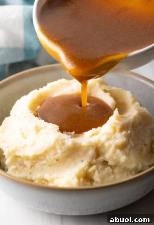 Delicious Homemade Beef Gravy 10 Pouring homemade beef gravy from a white pitcher over a bowl of mashed potatoes.