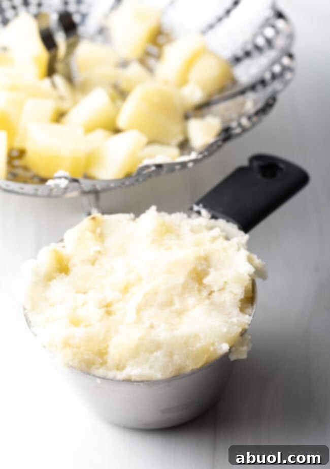 Metal measuring cup full of mashed potatoes.