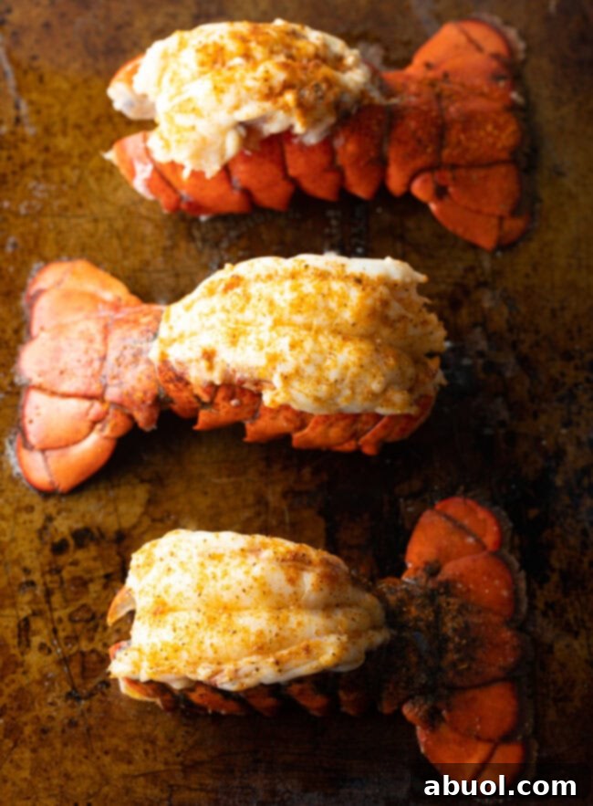 Top down view three plump cooked lobster tails on a baking sheet.