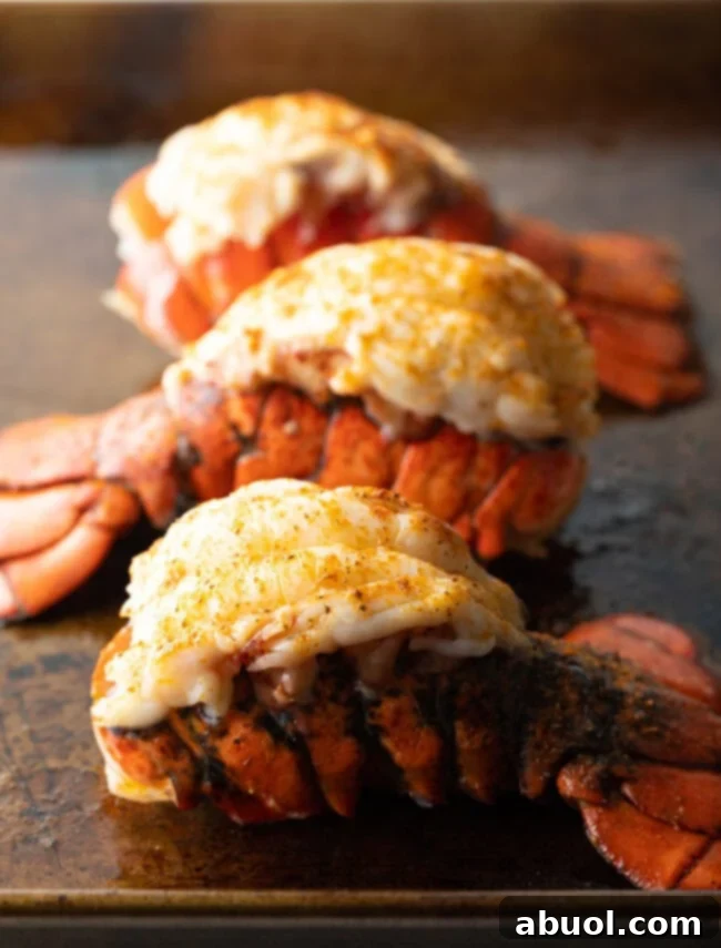 Three plump cooked lobster tails on a baking sheet.