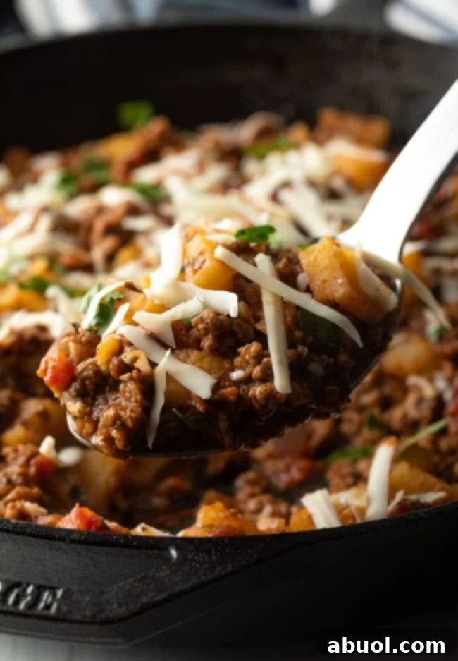 Metal spoon with potatoes and ground meat, topped with shredded parmesan cheese.