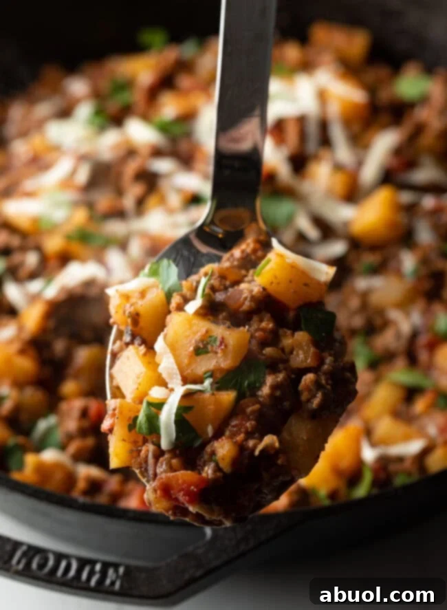 Metal spoon with ground beef and potatoes, topped with shredded parmesan cheese.