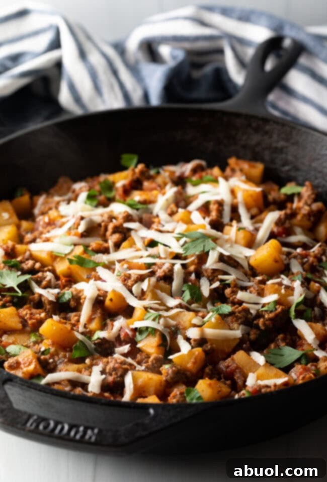 Ground meat and potatoes, topped with shredded parmesan cheese in a skillet.