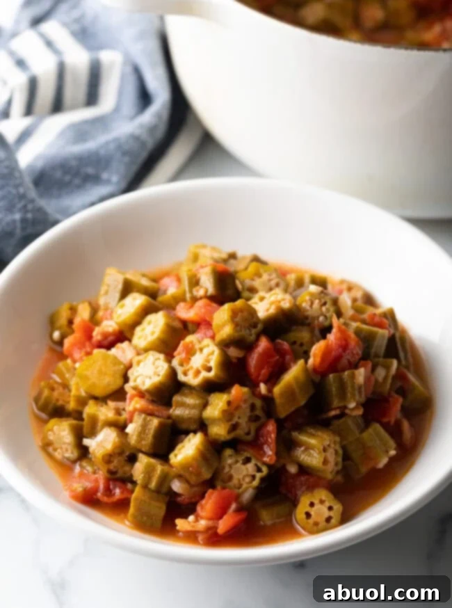 A vibrant white bowl generously filled with perfectly stewed okra and tomatoes, ready to be served.
