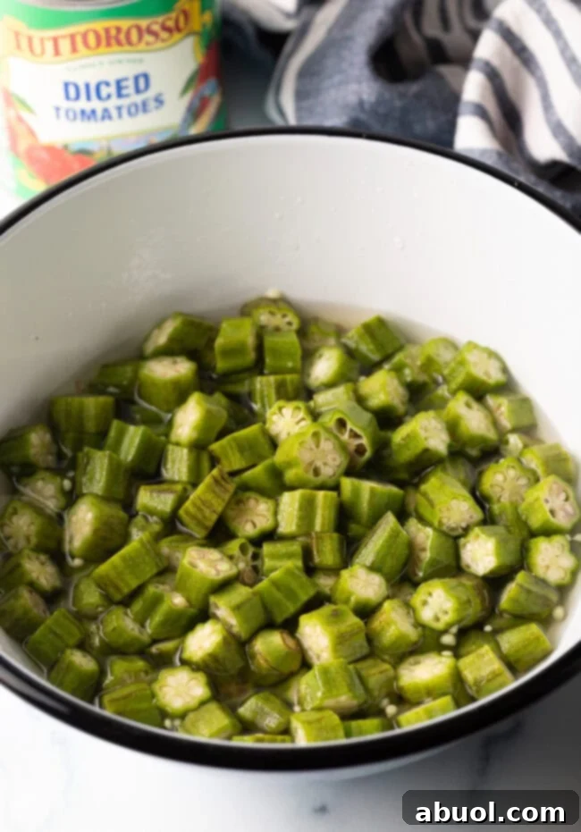 Close-up of chopped pieces of okra submerged in a clear vinegar and water solution within a glass bowl, illustrating the pre-soaking step.