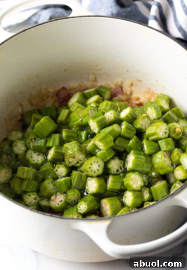 Chopped okra pieces added to a simmering pot with other vegetables, illustrating the next cooking stage.
