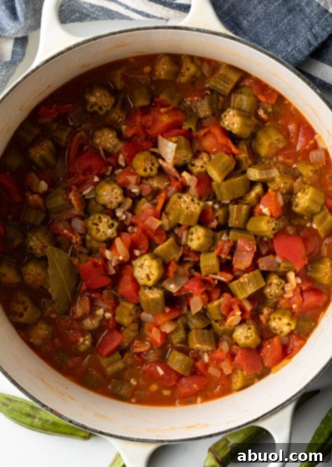 A top-down view of a white Dutch oven filled with rich, stewed tomatoes and okra, garnished and ready to serve.