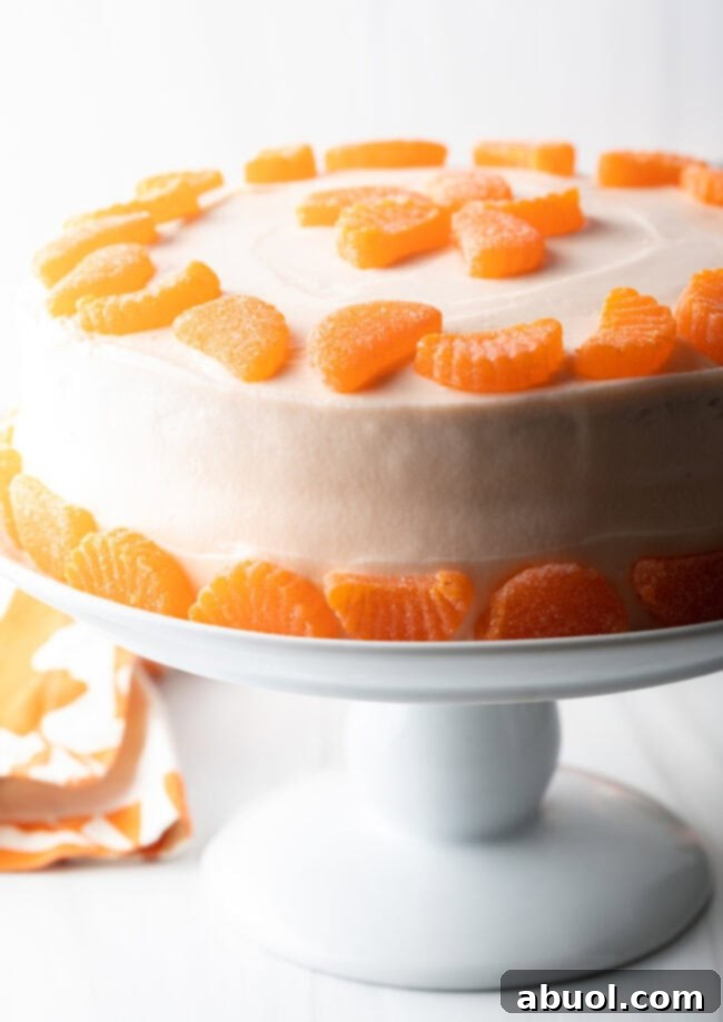 Side view of cake on a white pedestal. White frosting and ring of mandarin slices around the top and bottom of the cake.