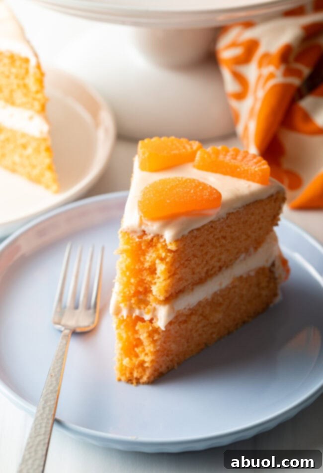 Slice of two layer orange crush cake on a white plate. Cake is decorated with a few slices of mandarin oranges, and a bite of the cake has been eaten.