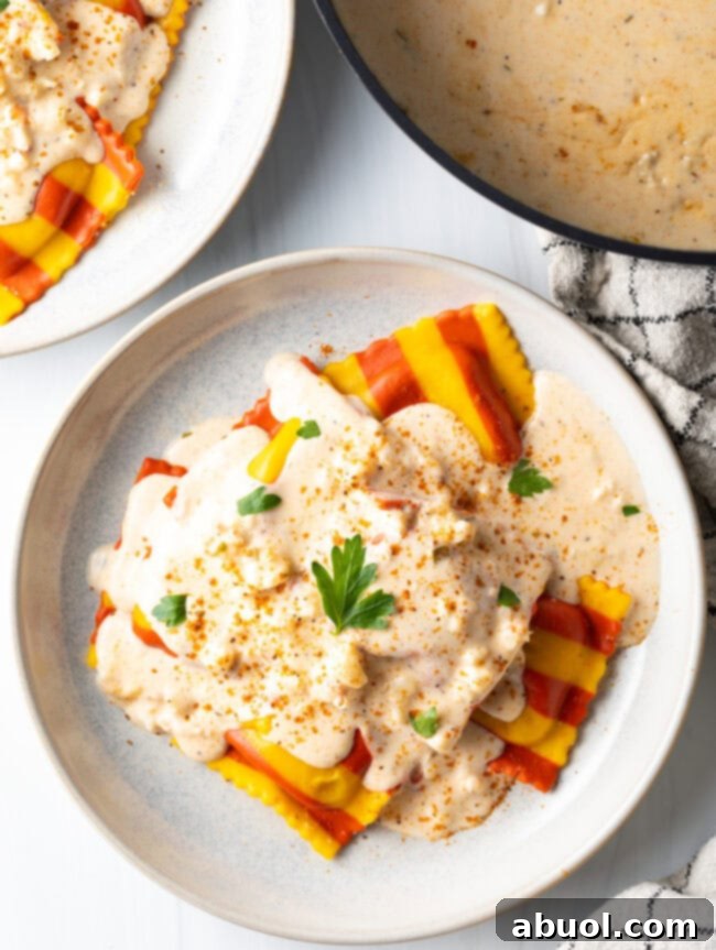 White plate with yellow and red striped ravioli, covered in creamy lobster sauce and sprinkled with parsley.