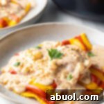White plate with yellow and red striped lobster ravioli, covered in a rich cream sauce and sprinkled with parsley.