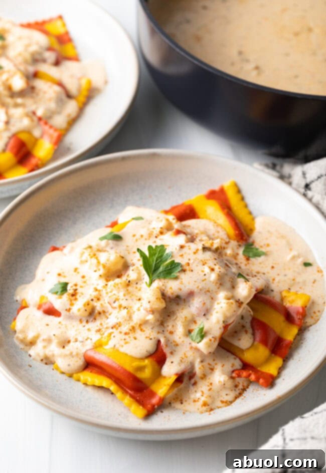 White plate with yellow and red striped lobster ravioli, covered in best sauce for lobster ravioli.