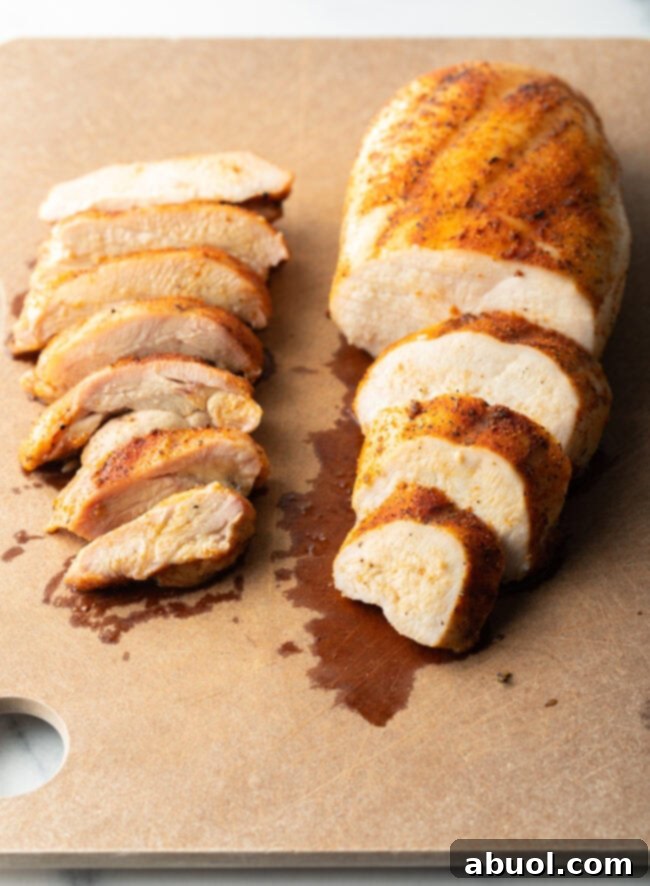 Close view of a smoked chicken breast and a chicken thigh on cutting board. Chicken breast is sliced into 4 large pieces. Thigh is sliced into 7 pieces.