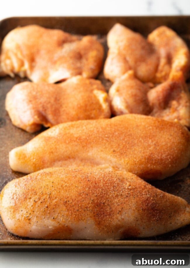 Raw chicken pieces with spices on a cutting board.