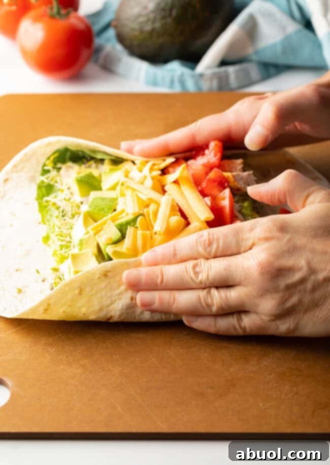 Two hands holding ingredients into the loaded tortilla while starting to roll into a wrap.