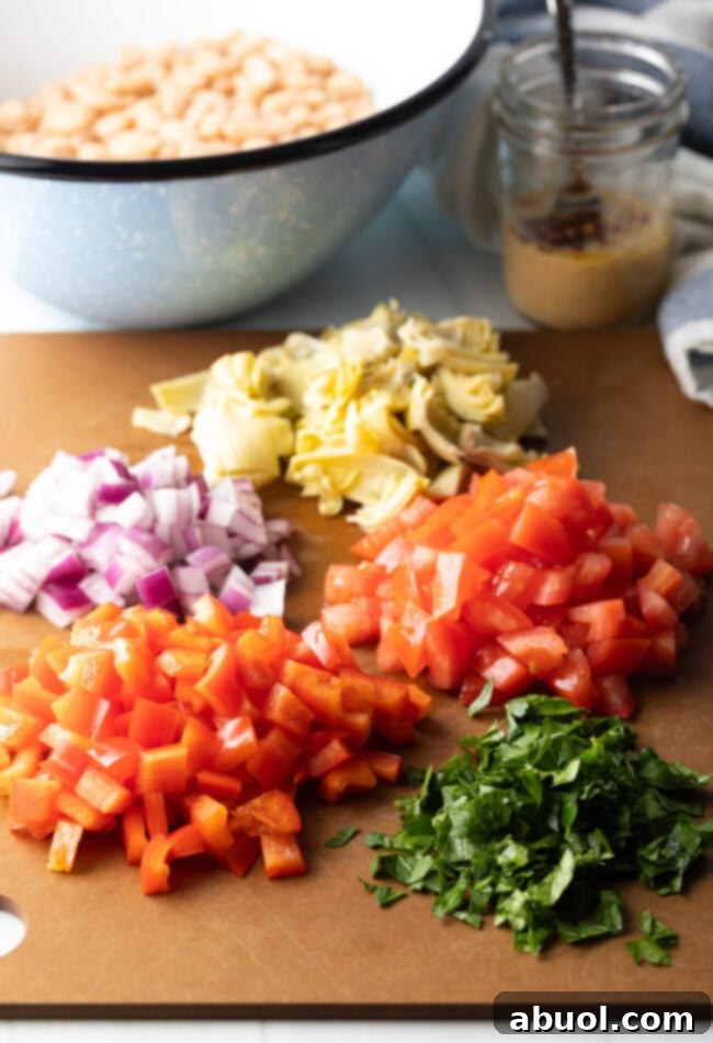Vibrant Artichoke White Bean Delight 4 Ingredients prep: chopped red onion, artichoke hearts, tomatoes, red bell pepper, and parsley neatly arranged on a brown cutting board.
