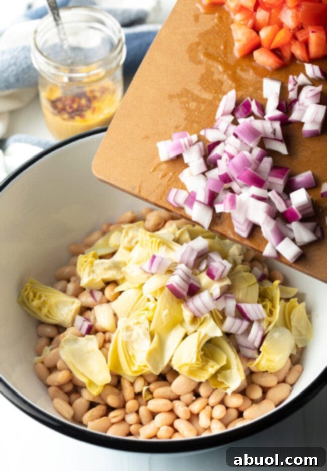 Vibrant Artichoke White Bean Delight 5 Adding artichoke hearts and diced onion to bowl with beans, beginning the salad assembly.