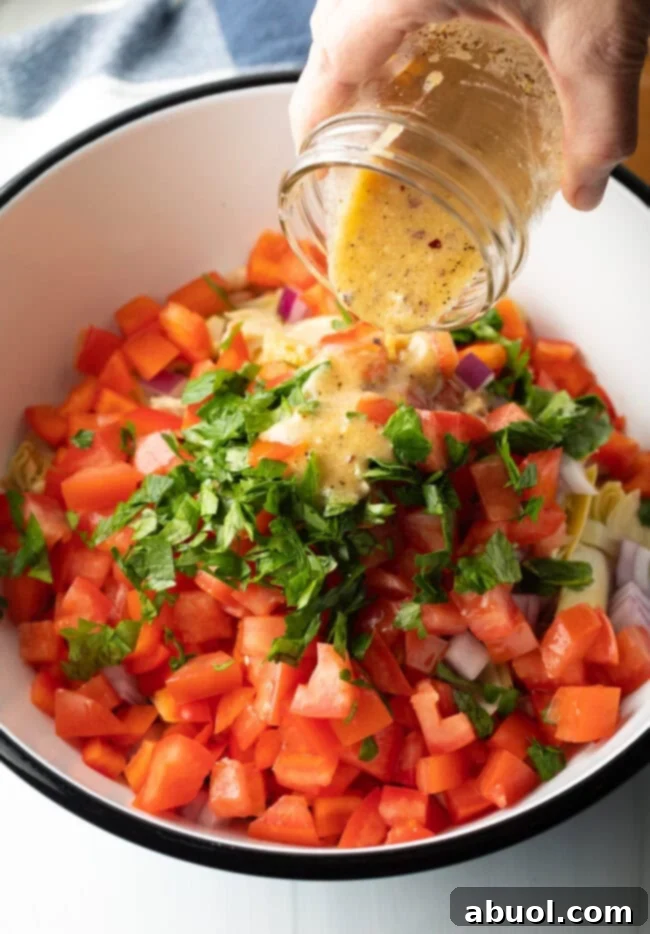Vibrant Artichoke White Bean Delight 7 Hand pouring vinaigrette dressing from a glass jar onto the chopped ingredients in a bowl, creating a perfect blend.