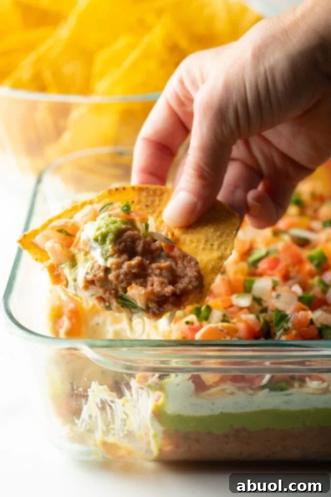 Close view of tortilla with a hand using a chip to scoop the 5 layer bean dip.