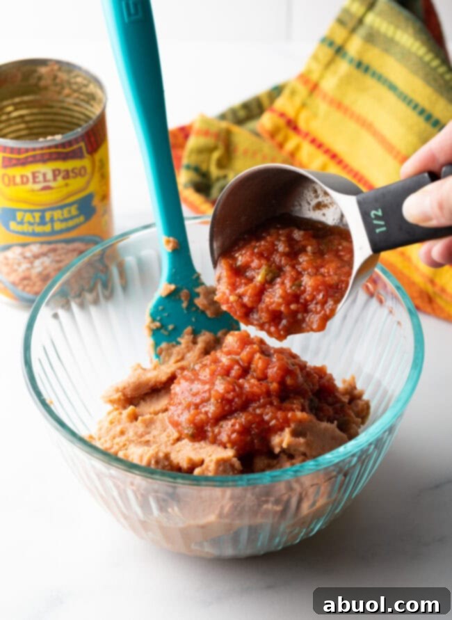 Hand with a measuring scoop adding salsa to a glass bowl.