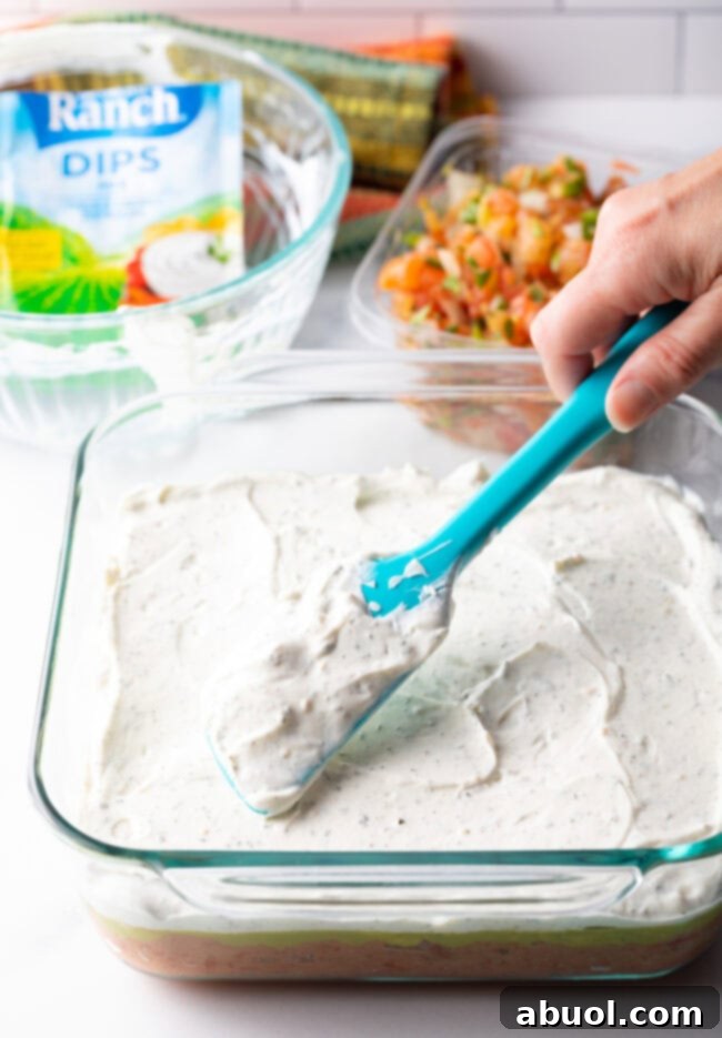 Hand with blue spatula spreading cream layer on.