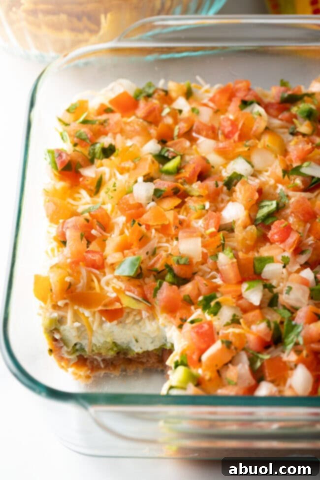View of glass dish with portion missing, showing all 5 layers of the Mexican bean dip.