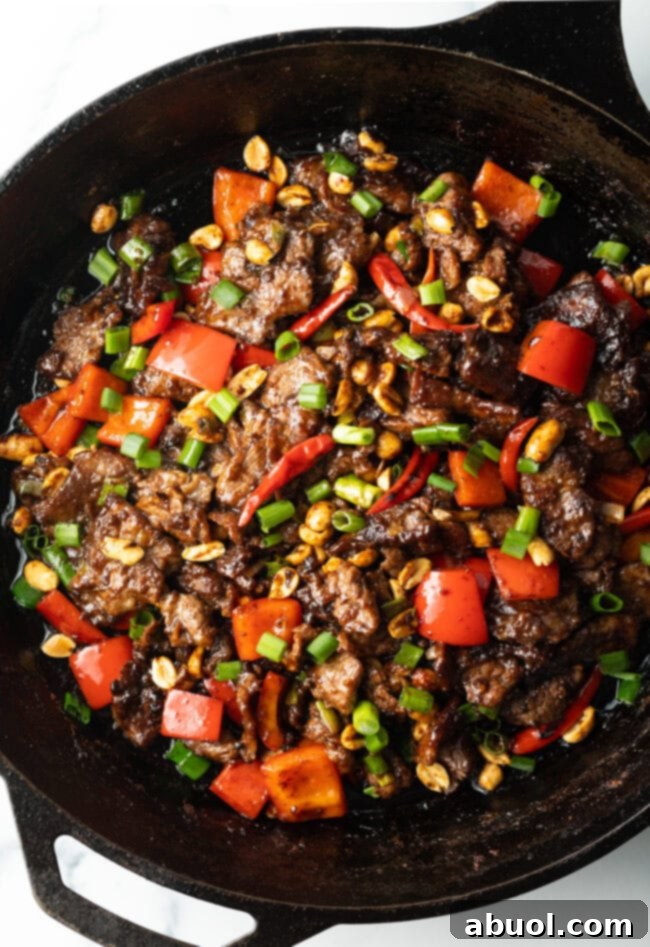 The finished Kung Pao Beef stir-fry, with tender beef, red bell peppers, and scallions, simmering in a cast iron skillet.
