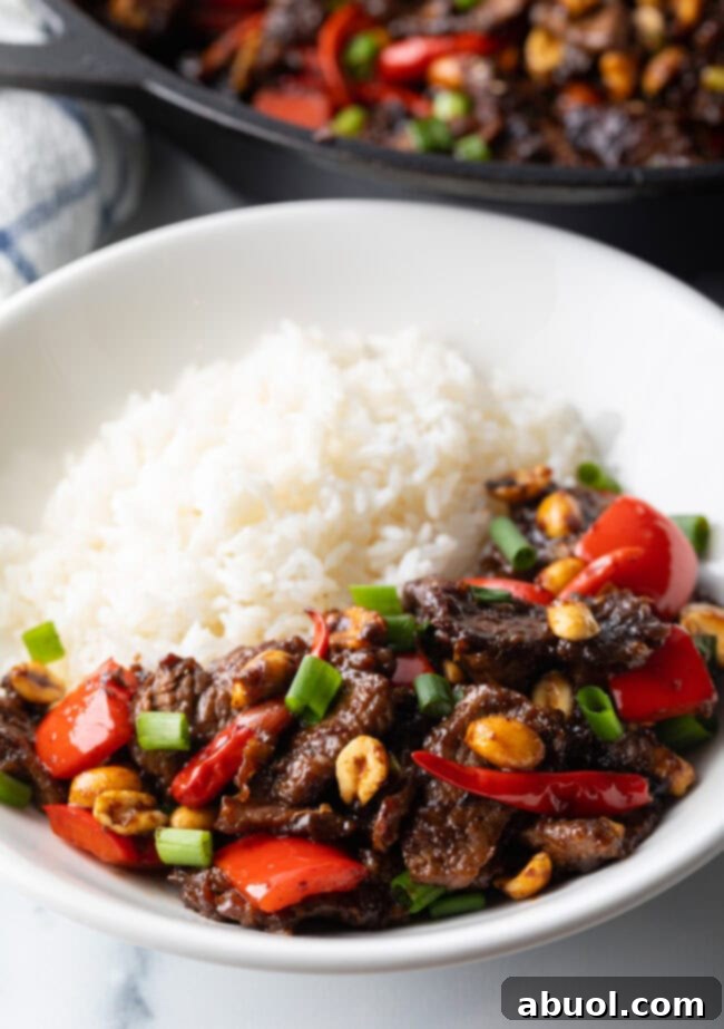 A close-up of Kung Pao Beef Stir Fry in a white bowl, served alongside white rice.