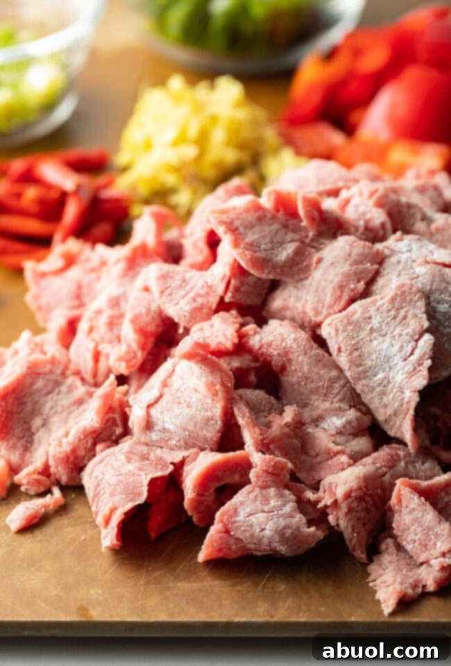 Recipe ingredients neatly chopped and organized on a cutting board: sliced flank steak, scallions, red bell peppers, minced garlic, and grated ginger.